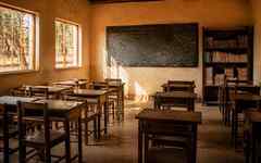 A sunlit empty African classroom with wooden desks and a blackboard